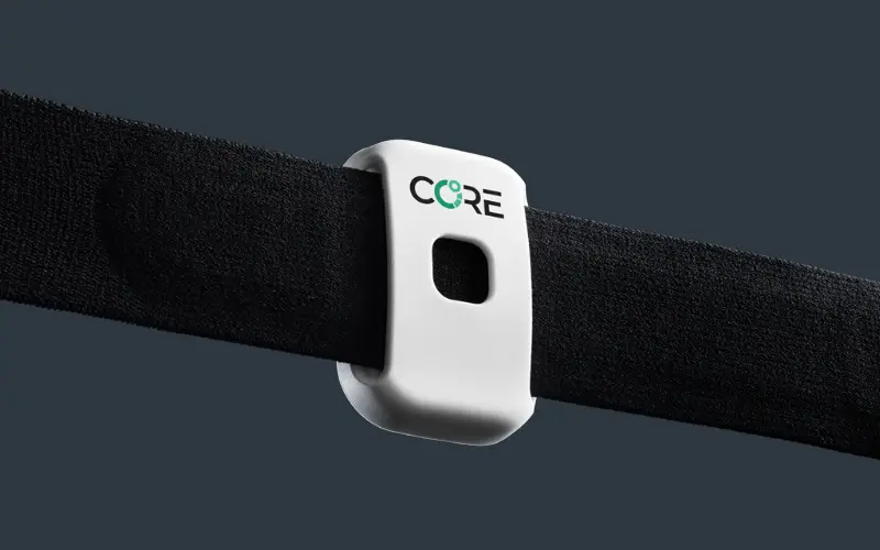 Nahaufnahme des weißen CORE-Körperkerntemperatur-Sensors mit Logo, der auf einem schwarzen Brustgurt befestigt ist.