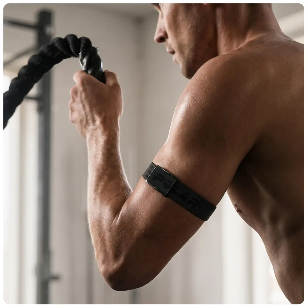 Dynamische Trainingsaufnahme eines Mannes mit Fitnessseilen. Am nackten Oberarm ist das dunkelgraue POLAR Loop Textilarmband mit eingeprägtem Polar-Schriftzug gut sichtbar, um eine präzise Herzfrequenzmessung beim Workout zu gewährleisten.