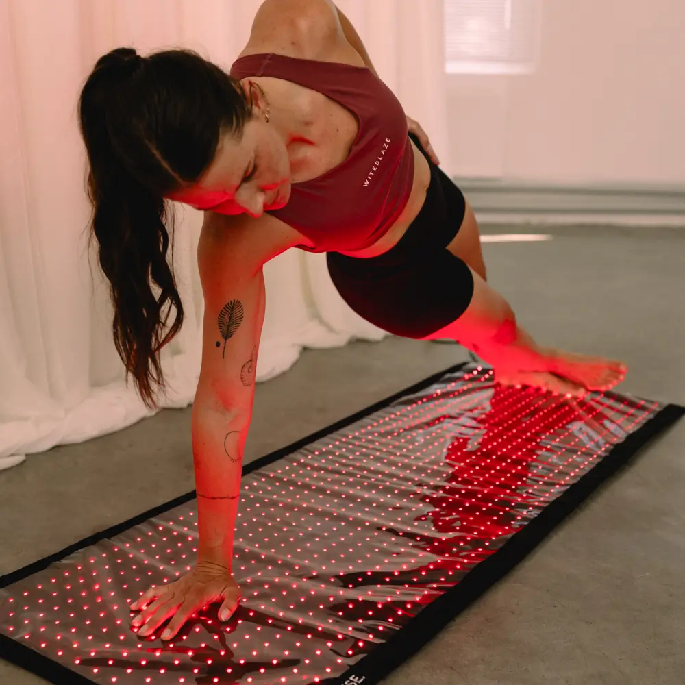 Eine Frau im Sportoutfit führt eine Side-Plank-Übung auf der rot leuchtenden Reboots Relight Rotlichtmatte aus.