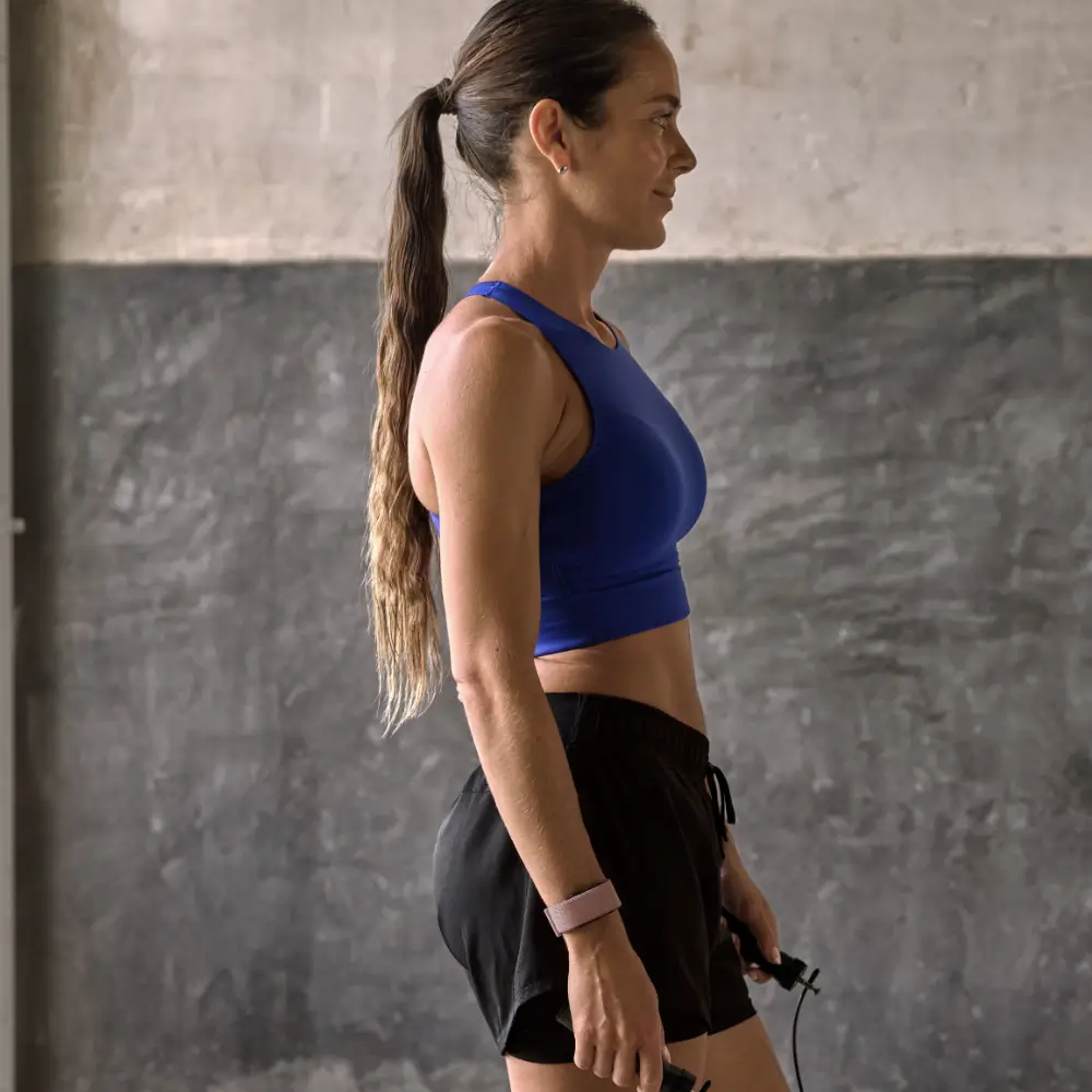 Eine Sportlerin im Seitenprofil trägt das Garmin Cirqa Smart Band in Malve am Handgelenk und hält ein Springseil beim Fitness-Workout