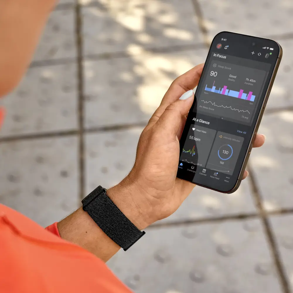 Garmin Cirqa Smart Band in Schwarz am Handgelenk einer Person, die Gesundheitsdaten wie Schlaf-Score und Herzfrequenz in der Garmin Connect Smartphone-App abliest